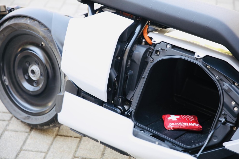 Prtljažnik pod sedežem. Enostaven dostop in uporabna oblika. Za njim se pod belo plastiko skriva elektromotor, baterije so nameščene v dnu skuterja.