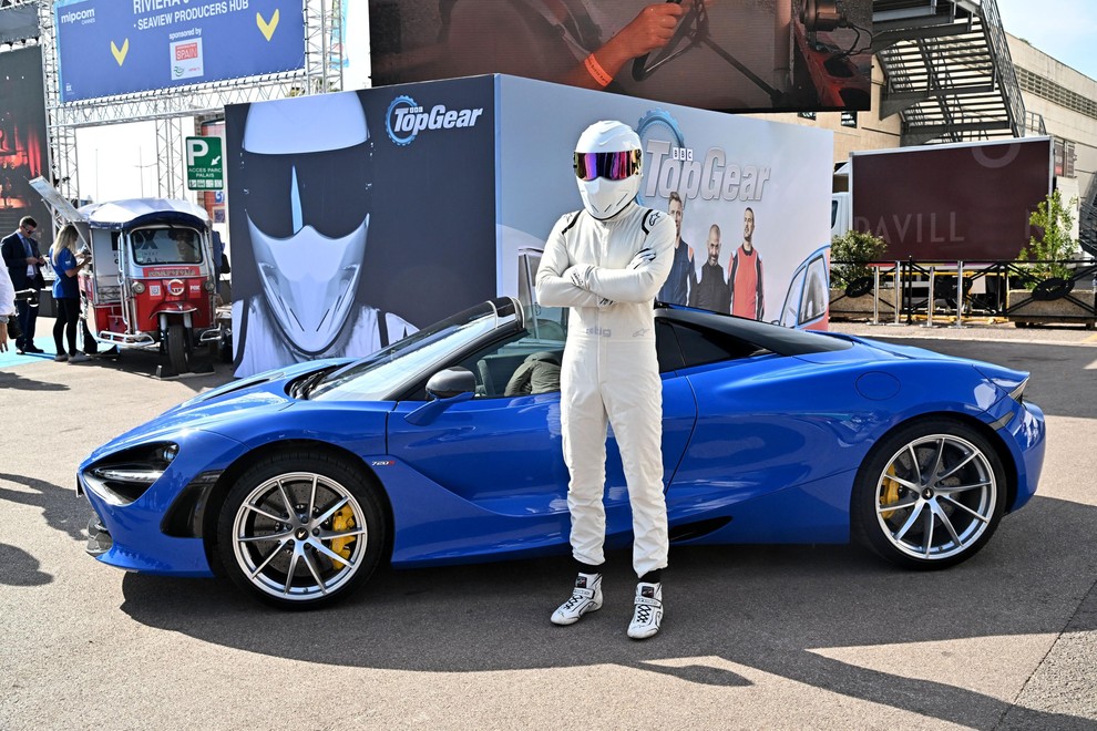 Voznik Stig iz oddaje top Gear stoji pred modrim avtomobilom